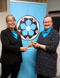 Tiina Ronkainen ojentaa puheenjohtajan nuijan Mirja Airokselle. 