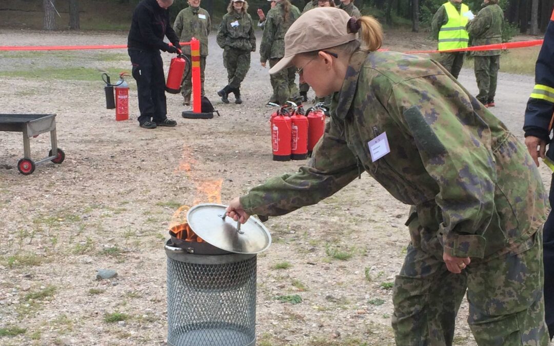 Maastoasuinen nainen sammuttaa rasvapaloa kattilan kannella ulkona.